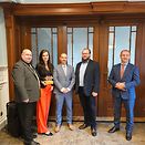 Five people in front of a door. One of these people holds an award in her hand.
