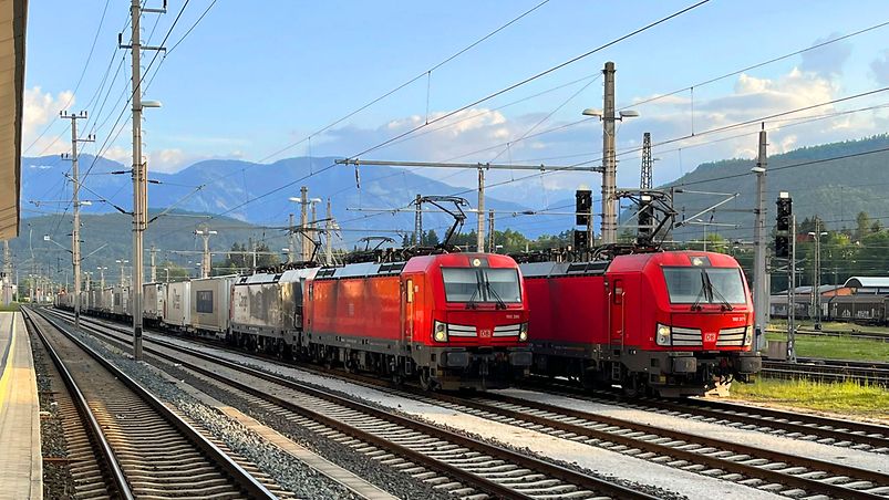 two trains with red locomotives in front of mountains